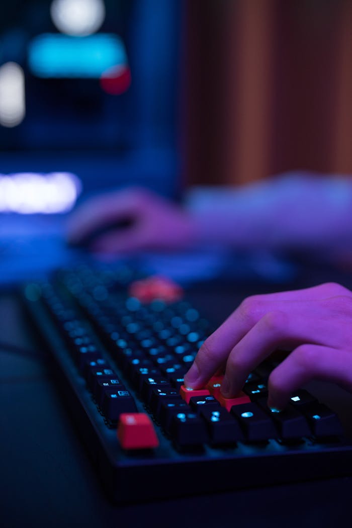 Hands typing on an RGB gaming keyboard in a moody, dimly lit room.