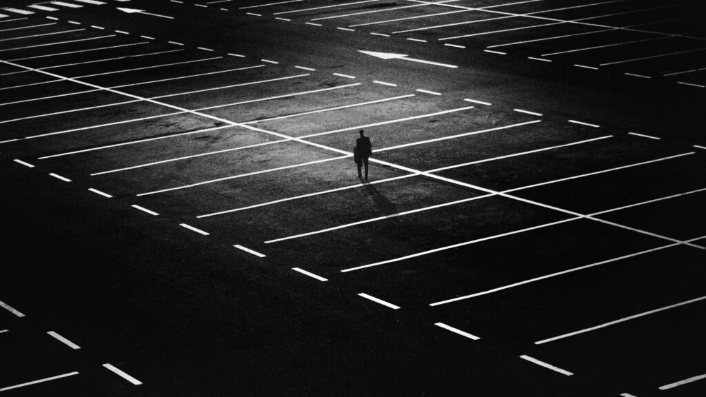 Silhouette of a solitary figure in an expansive night-time parking lot.